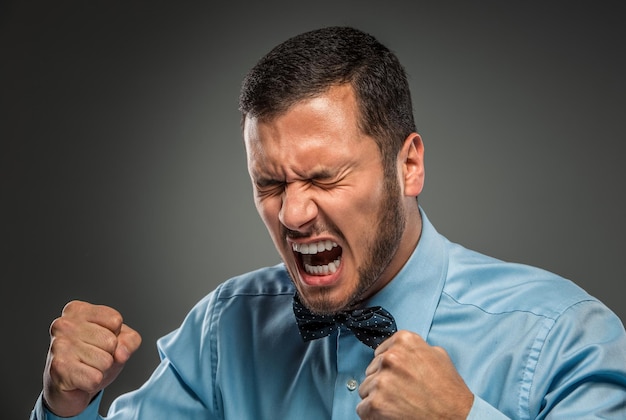 Foto portret boos overstuur jonge man in blauw shirt, vlinderdas