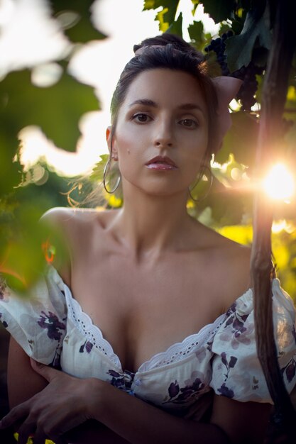 Portret brunette vrouw in een witte jurk staat in een wijngaard in de zomer in Italië