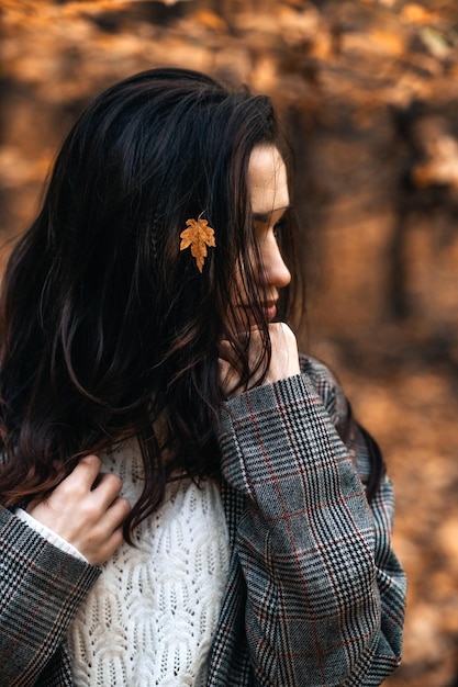 Portret brunette vrouw met herfst gele bladeren in lang haar op herfst natuur achtergrond