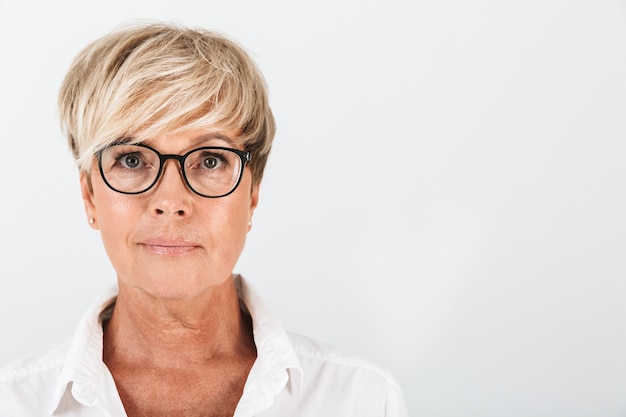 Portret close-up van een blanke vrouw van middelbare leeftijd die een bril draagt en naar een camera kijkt die over een witte muur in de studio is geïsoleerd