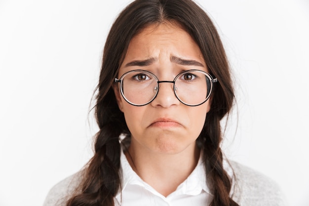 Portret close-up van gefrustreerd boos meisje met een bril die huilt en fronst met een droevig gezicht geïsoleerd over een witte muur