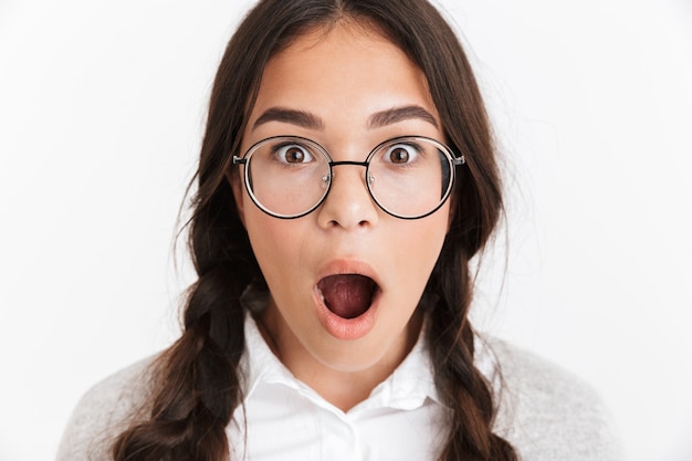 Portret close-up van verbaasd tienermeisje met een bril en schooluniform zich af met open mond geïsoleerd over witte muur