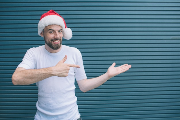 Portret dat van de gelukkige en mens zich aan het recht bevindt poiting. Hij draagt een kerstmuts. Guy kijkt op camera en lacht. Geïsoleerd op gestreept