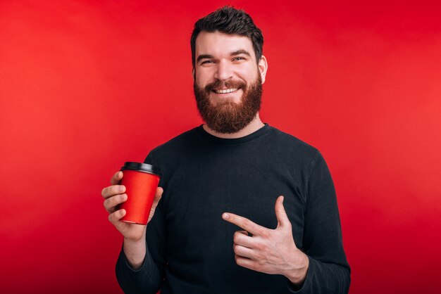 Portret dat van de gelukkige mens zich over rode ruimte bevindt en op kop van koffie richt om te gaan