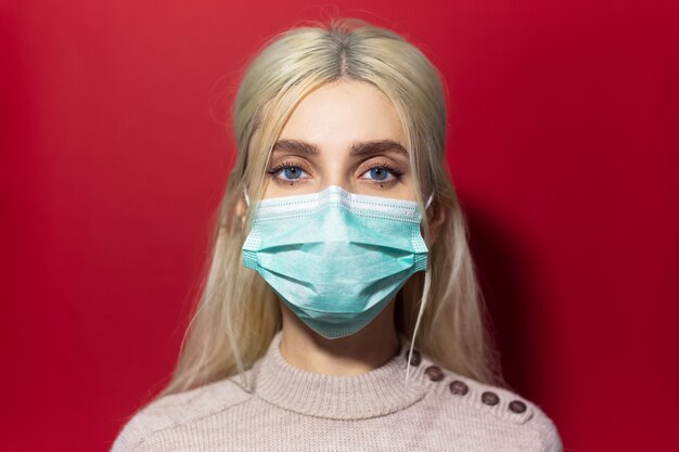 Portret dat van jong blondemeisje met blauwe ogen, het masker en de sweater van de griepmedicijn draagt