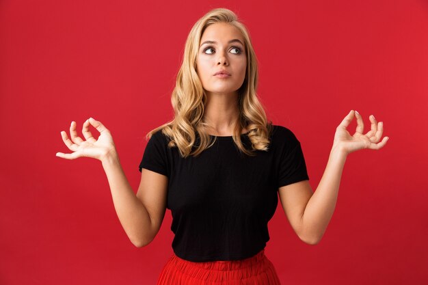 Portret dat van jonge vrouwen20s vingers voor meditatie samenhoudt, over rode muur wordt geïsoleerd