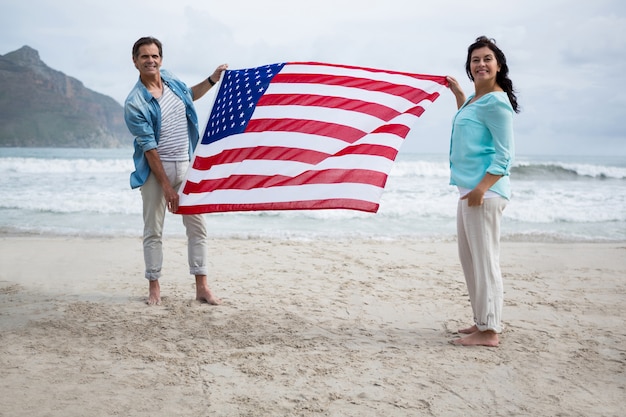 Portret dat van paar Amerikaanse vlag op strand houdt