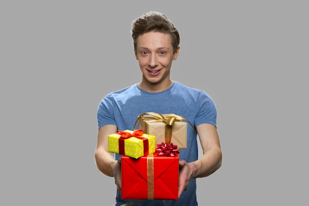 Portret dat van tiener giftdozen aanbiedt. Knappe tiener man met geschenkdozen op grijze achtergrond. Verjaardag cadeau concept.