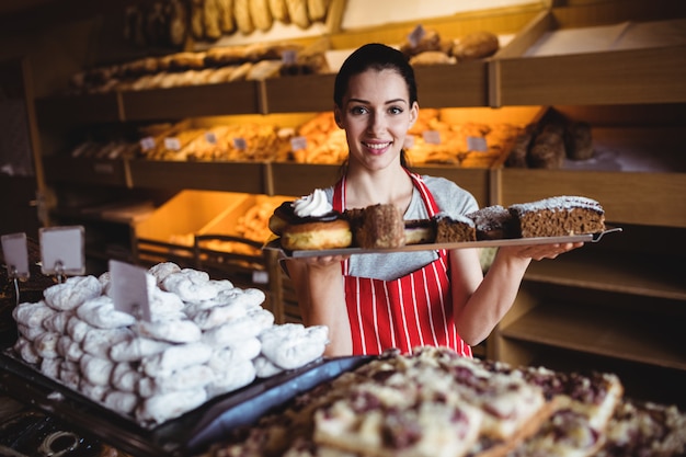 Portret dat van vrouwelijke bakker een dienblad van zoet voedsel houdt