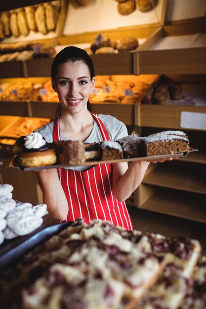 Portret dat van vrouwelijke bakker een dienblad van zoet voedsel houdt