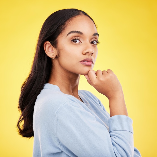 Portret denken en een vrouw op een gele achtergrond in de studio die zich bedachtzaam of contemplatief voelt Gezichtsidee en een aantrekkelijke jonge vrouw staande hand op kin terwijl ze een gedachte overweegt