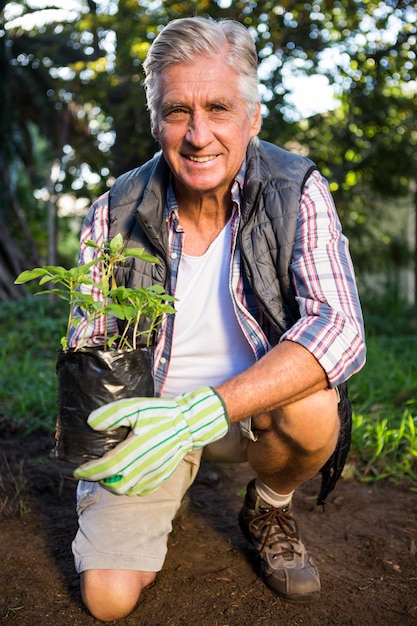 Portret die van gelukkige tuinman met ingemaakte installatie knielen bij tuin