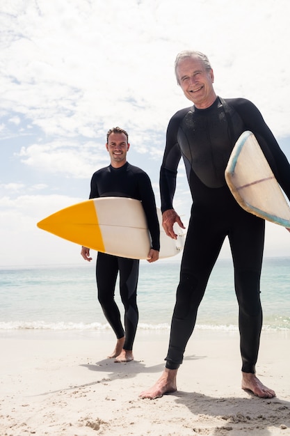 Portret die van gelukkige vader en zoon zich met surfplank op het strand bevinden