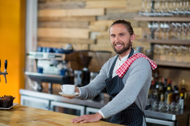 Portret die van glimlachende kelner kop van koffie aanbieden