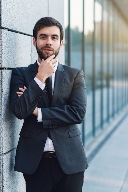 Portret die van jonge zakenman een baard in pak het stellen houden op achtergrond van de bureaubouw
