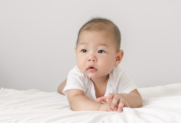 Foto portret die van weinig kleine aziatische babyzuigeling die op bed leggen omhoog eruit zien