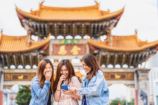 Portret drie aziatische geluksvrouwen die en slimme mobiele telefoon lachen met behulp van