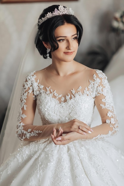 Foto portret een brunette bruid in een trouwjurk met lange kant mouwen en een chique kroon staat te poseren prachtige make-up en haar voluminous sluier wedding foto mooie bruid