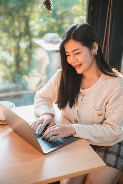 Portret freelance bedrijf mooie positieve glimlach jonge Aziatische vrouw meisje draagt warme kleding online werken met laptopcomputer met koffiekopje mok thuis thuis in de woonkamer binnen of café