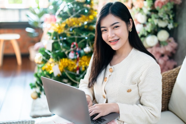 Portret freelance zakelijke glimlach jonge Aziatische vrouw met kopje koffie online werken met laptopcomputer thuis in de woonkamer binnenshuis Decoratie tijdens Kerstmis, Kerstmis en Nieuwjaar vakantie