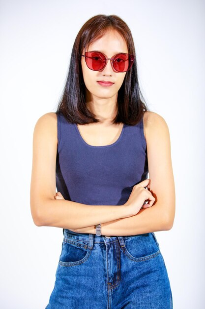 Portret geïsoleerd close-up studio knipsel shot van Aziatische vrouwelijke model in crop top shirt jeans en zonnebril glimlachend camera kijken op witte achtergrond