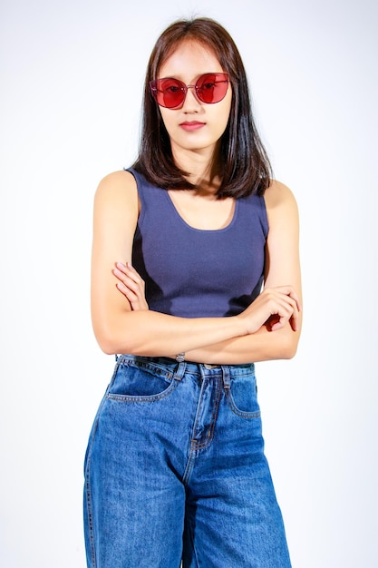 Portret geïsoleerd close-up studio knipsel shot van Aziatische vrouwelijke model in crop top shirt jeans en zonnebril glimlachend camera kijken op witte achtergrond