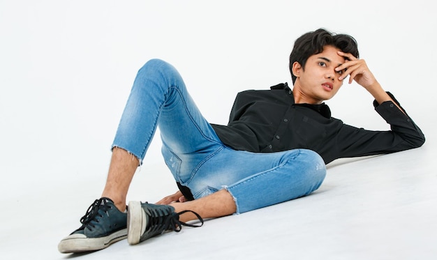 Portret geïsoleerd knipsel studio shot van Aziatische jonge Lgbtq gay glamour mannelijk model in casual zwart shirt en jeans outfit zittend uitrekken poseren gebaren op verdieping kijken naar camera op witte achtergrond