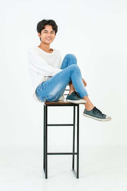 Portret geïsoleerde studio opname Aziatische jonge Lgbt homo gelukkig knappe biseksuele homoseksuele mannelijke mannequin in casual outfit zittend gekruiste benen op hoge stoel glimlachend kijken naar camera op witte achtergrond