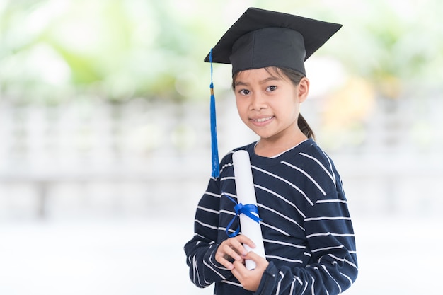 Portret gelukkige Aziatische vrouwelijke schooljongen afgestudeerd in een afstudeerpet heeft een opgerold certificaat. Afstuderen Viering Concept Stock Photo