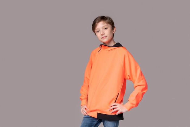 Portret gelukkige blanke tiener man in oranje sweatshirt op grijze kleur