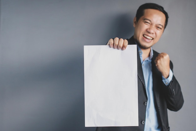 Portret gelukkige succesvolle zakenman houdt in de hand leeg wit vel op grijze achtergrond Plaats voor