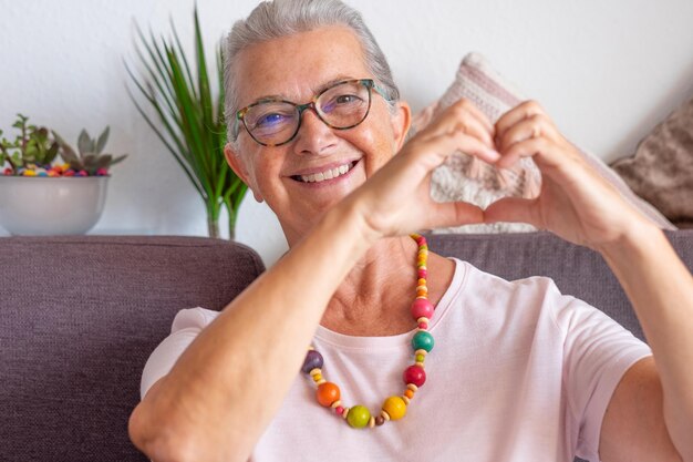 Portret gelukkige volwassen volwassen oudere vrouw die een bril draagt en een hartgebaar maakt met vingers