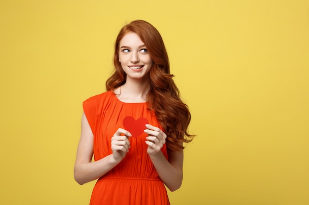 Portret gelukkige vrouw die een hartsymbool op gele achtergrond houdt.