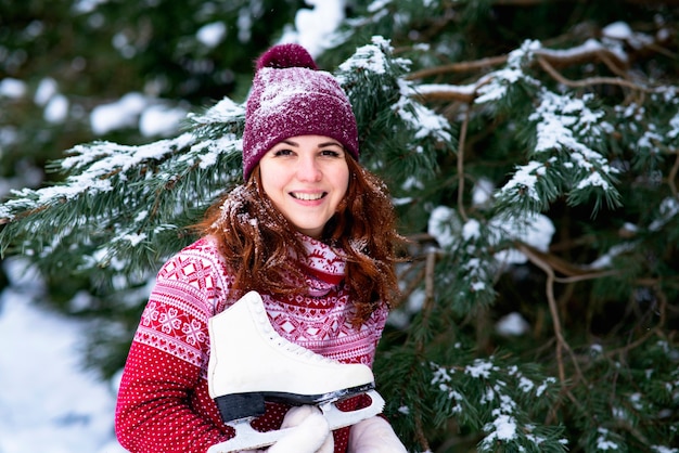 Portret. Gelukkige vrouw met winter skates op haar schouder in een besneeuwd bos. Winterpret en sport.