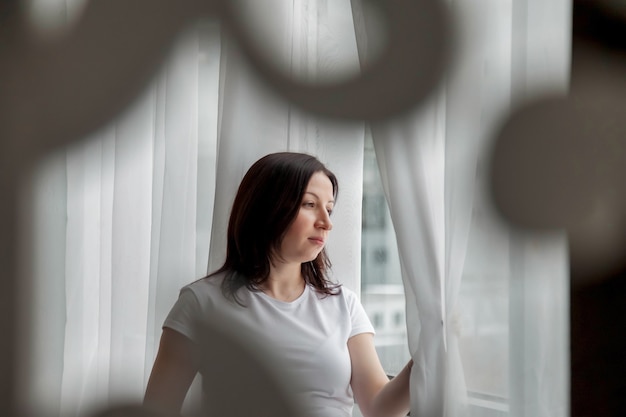 Portret gelukkige zwangere vrouw met grote buik bij raam in huis. Zwangerschap, moederschap, mensen en verwachtingsconcept. Sfeervolle familiemomenten. Ruimte kopiëren