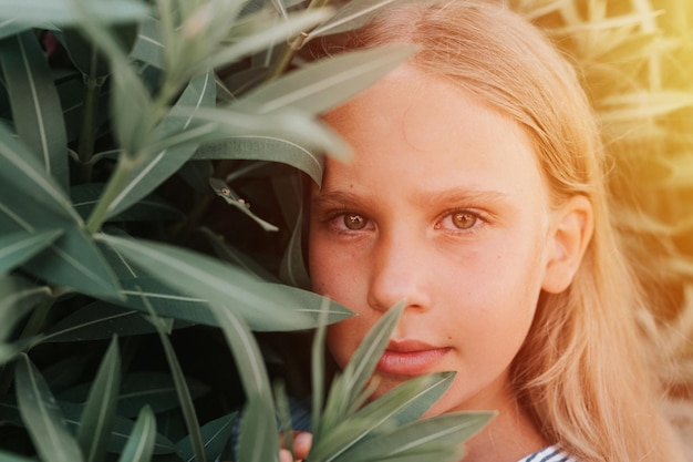 Portret gezicht van openhartig gelukkig klein kind meisje van acht jaar oud met lang blond haar en groene ogen op de achtergrond van groene planten tijdens een zomervakantie reizen gen z geestelijke gezondheid concept flare