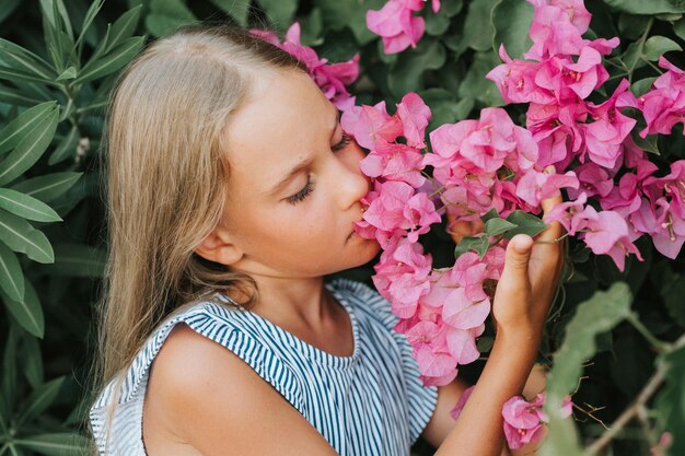 Portret gezicht van openhartig klein meisje van acht jaar oud op de achtergrond van groene planten en bewonderd genieten van geur roze bloemen tijdens een zomervakantie reizen gen z geestelijke gezondheid concept