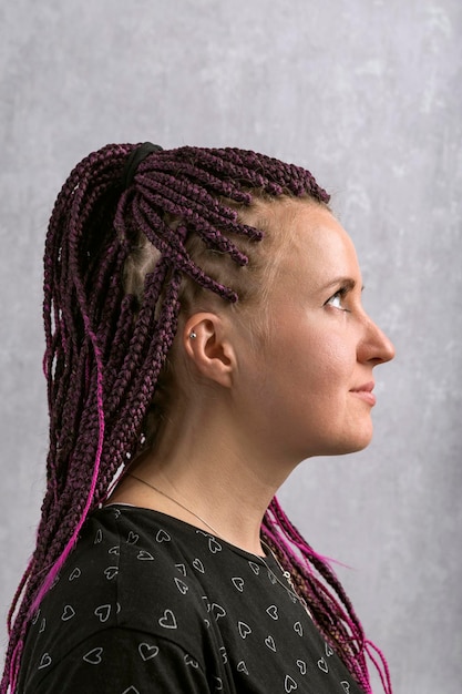 Portret in profiel van jonge vrouw met vlechten op grijze achtergrond Informeel freaky meisje draagt dreadlocks Verticaal frame