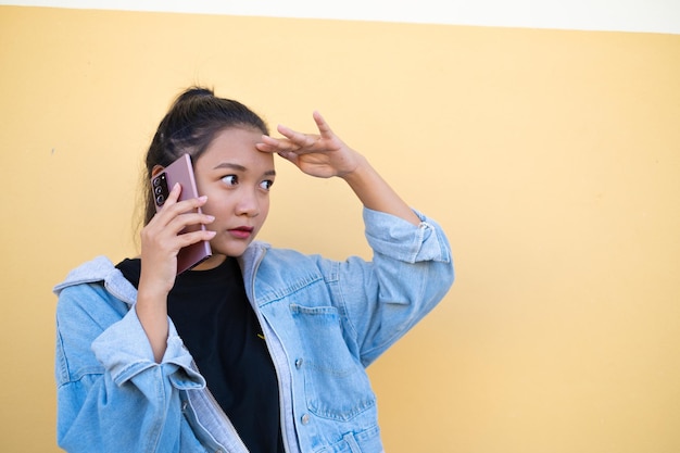 Portret jong meisje draag jas jean en gebruik mobiel op bruine achtergrond.