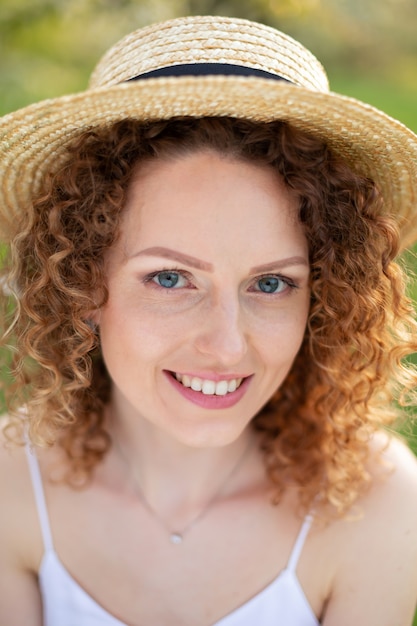 Portret jonge aantrekkelijke vrouw met krullend haar in een stijlvolle rieten hoed in een groene tuin