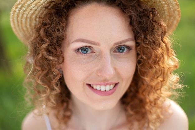 Portret jonge aantrekkelijke vrouw met krullend haar in een stijlvolle rieten hoed in een groene tuin