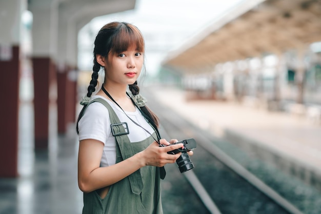 Portret jonge aziatische vrouw die lacht toerist reiziger meisje wandelen en met een holding de camera wacht trein reizen reis wordt genomen in spoorwegplatform Thailand zomer ontspannen vakantie Concept