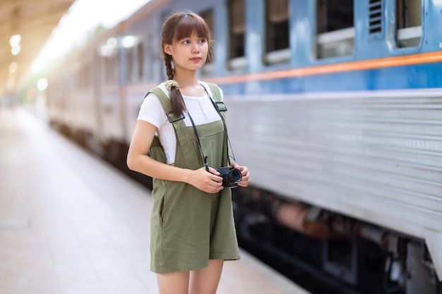 Portret jonge aziatische vrouw die lacht toerist reiziger meisje wandelen en met een holding de camera wacht trein reizen reis wordt genomen in spoorwegplatform Thailand zomer ontspannen vakantie Concept