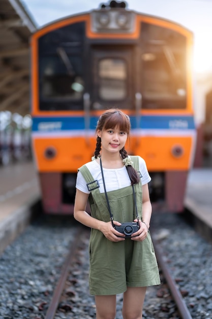 Portret jonge aziatische vrouw die lacht toerist reiziger meisje wandelen en met een holding de camera wacht trein reizen reis wordt genomen in spoorwegplatform Thailand zomer ontspannen vakantie Concept