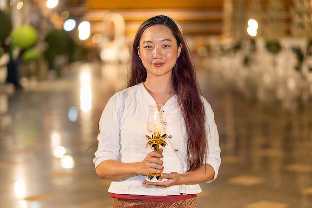 Portret jonge aziatische vrouw lacht en draagt traditionele kleding van Thailand met kaars in Wat Suthat Thepwararam