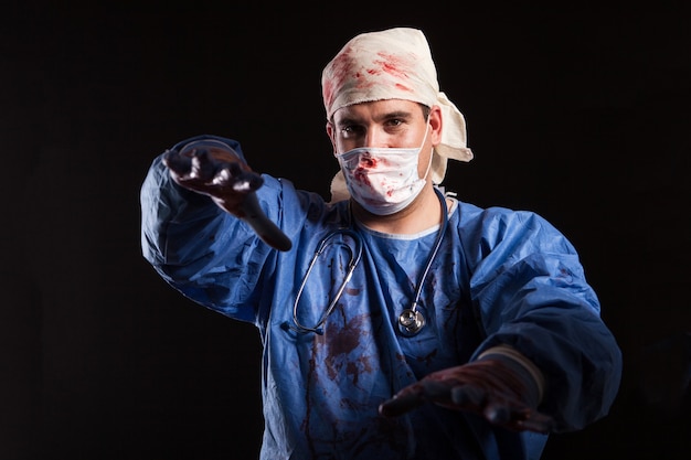 Portret jonge man in gekke dokterskleren die met zijn handen over zwarte achtergrond reiken voor halloween-carnaval. Gefrustreerde dokter met sinistere blik.
