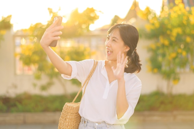 Portret jonge mooie aziatische vrouw die smartphone gebruikt om te videobellen met vriend en straat te verkennen op zomervakantie in Bangkok, Thailand