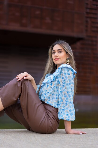 Portret jonge vrouw zittend in de stad tegen een ijzeren achtergrond met bruin roest lifestyle concept blauw shirt en bruine broek