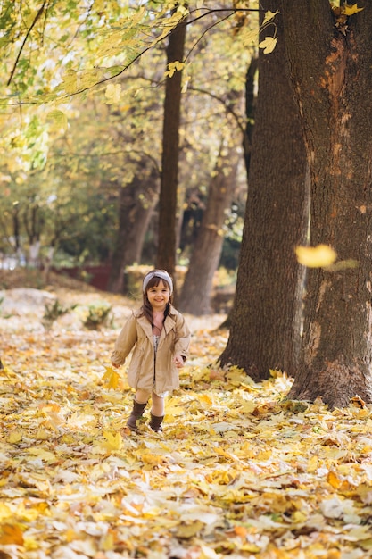 portret klein meisje in een beige jas loopt in de herfst park