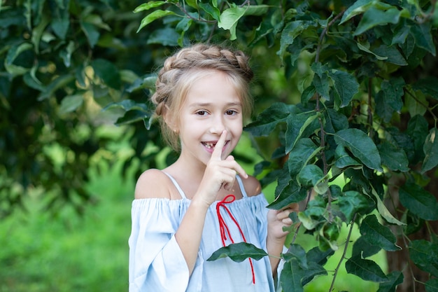 portret klein meisje met staartje op haar hoofd staat in groen gebladerte in de tuin kind op de boerderij